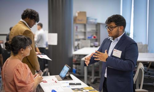 A WPI student wearing a suit stands behind a table and presents their innovation